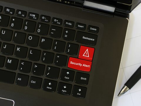 Laptop on workspace with red keyboard key with the word security alert on it. Cyber security concept